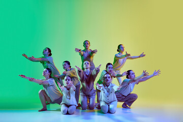 Group of young adorable girls moving to the beat of the music on gradient background in neon light. Teenage choreography studio