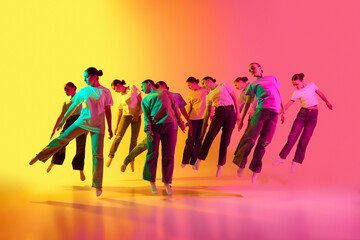 Group of teenagers, young dancers standing in a row and jumping up on pink and yellow background in neon light. Creative improvisation
