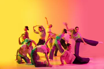 Fotobehang School girls wearing white clothes dancing together on pink and yellow gradient background in neon light. Choreography figures © Lustre Art Group 