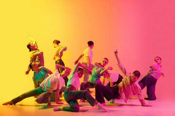 Group of teenagers, young dancers emotionally dancing together on pink and yellow gradient...
