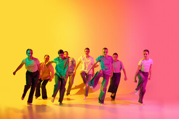 Portrait with group of teenagers, young dancers jumping together over pink and yellow gradient background in neon light. Modern dance style