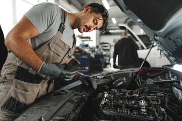Fototapeta na wymiar Young male mechanic examining engine under hood of car at the repair garage