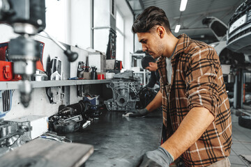 Young man mechanic repairing car parts on worktable in car service shop