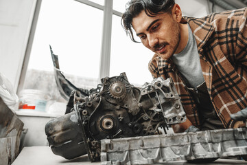 Workman disassembling car engine at the working table of the car service garage