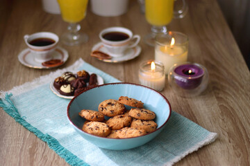 Plate of chocolate pralines, bowl of cookies, cups of tea, glasses of juice and lit candles on the table. Selective focus.