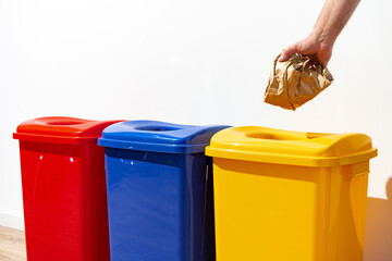 Hand putting crumpled paper into a color trash bin