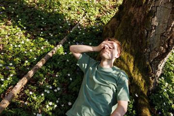 Young man laying in green grass with flowers. People fatigue from work. Summer sleeping and relaxation techniques. Vitamin D sunbathing. Man power nap with eye closed. Rest after work from home