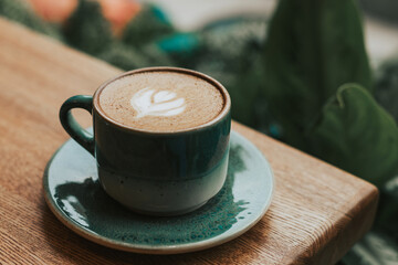 Cappuccino with latte art in a green ceramic mug on a wooden table. Delicious coffee with alternative milk. Double Cappuccino for breakfast