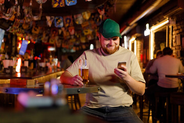 a guy in a cap sits in a bar and uses a mobile
