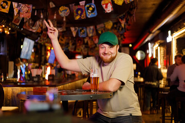 portrait of a cheerful red-haired guy with a beer at a table in a pub makes an order