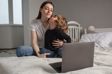 Happy mother with her little son enjoying in online shopping or working from home. Business from distance and virtual communication. Mom and baby watch cartoons or play game on laptop on the bed.