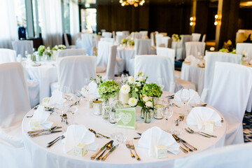 Festsaal bei einer Hochzeitsfeier im Restaurant mit Gedeck und weißer Tischdecke und Blumenschmuck