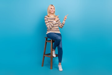 Fototapeta premium Full length photo of pretty nice lady sit chair look indicate fingers empty space information isolated on blue color background