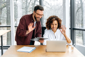 Successful coworkers of different nationalities, a man and a woman, working together, discuss business goals and ideas for new project with partners by video call, smile. Online video conversation