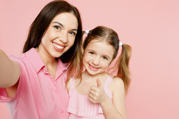 Close up happy woman wear casual clothes with child kid girl 6-7 years old. Mother daughter do selfie shot pov on mobile cell phone isolated on plain pastel pink background. Family parent day concept.