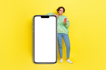 Full length photo of cheerful sweet lady wear hoodie reading apple samsung modern gadget empty space isolated yellow color background