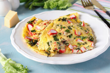 Omelet with crab sticks, cheese and green onions on a white plate on blue background. Close-up