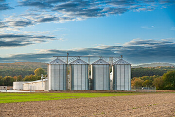 Fototapeta na wymiar plowed field with silver silos and a farmhouse at the horizon