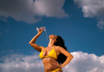 Sensual girl pouring wine from crystal glass on her body, dressed in bikini, artistic image 