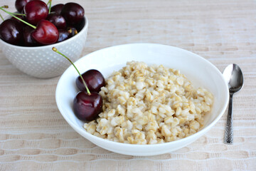 A bowl of porridge with two cherries and bowl of cherry in the background 