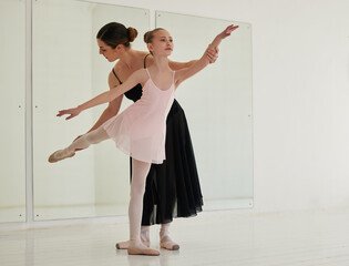 Learning a valued art form. a young girl practicing ballet with her teacher in a dance studio.