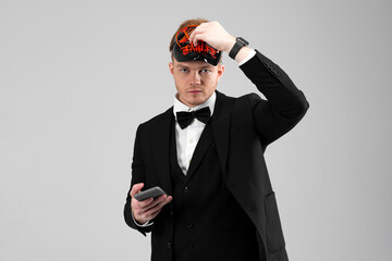 Stylish young man in a sharp black formal suit wearing a bright face mask, holds a phone. Concealed...