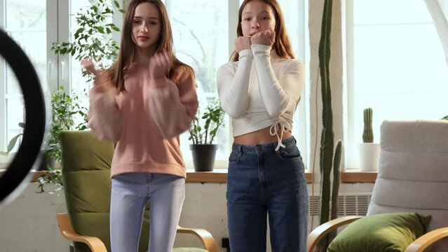 Two beautiful teen girls, friends in casual clothes recording video with mobile phone, dancing for social media publication. Concept of social media, blogging, modern technologies, influence