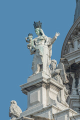Fototapeta na wymiar Ancient sculpture of beautiful Venetian Noble Renaissance Era woman with child at Basilica di Santa Maria della Salute in Venice, Italy, at blue sky