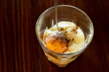 Soft-boiled eggs in glass with seasoning sauce and ground pepper; Thai breakfast vintage style. 