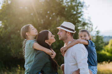 Portrait of young couple with their daughters in the nature, kissing. Side view.