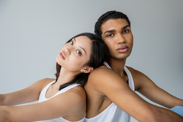 brunette asian woman and stylish african american man with silver piercing sitting back to back...