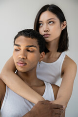 Obraz premium charming asian woman hugging young african american man with silver piercing isolated on grey.