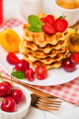 Stack of belgian waffles with fresh strawberries, cherry and apricot on white plate