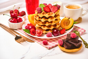Healthy Breakfast set with Belgian waffles with strawberries, apricots, cherries, juice and a cup of black coffee and bitter chocolate on white stone table background