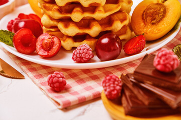 Healthy Breakfast set with Belgian waffles with strawberries, apricots, cherries, juice and a cup of black coffee and bitter chocolate on white stone table background