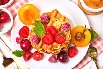 Healthy Breakfast set with Belgian waffles with strawberries, apricots, cherries, juice and a cup of black coffee and bitter chocolate on white stone table background