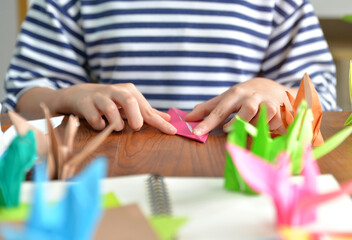 Female hands folding paper birds colorful as a hobby on a wooden table at home