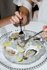 Hands of a young girl with utensils close-up eating oysters in a restaurant