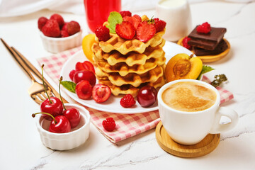 Healthy Breakfast set with Belgian waffles with strawberries, apricots, cherries, juice and a cup of black coffee and bitter chocolate on white stone table background