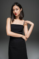 Fototapeta premium charming asian woman in black elegant dress looking at camera on grey background.