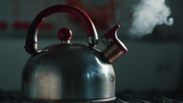 A boiling kettle with a whistle,standing on a gas stove and letting off steam