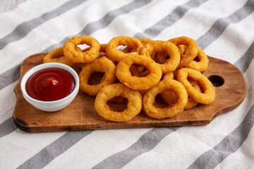 Homemade Crispy Deep-Fried Onion Rings with Ketchup on a rustic wooden board, low angle view.