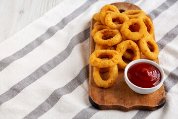 Homemade Crispy Deep-Fried Onion Rings with Ketchup on a rustic wooden board, low angle view. Copy space.