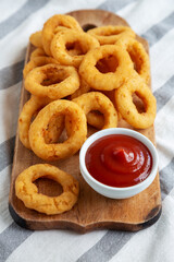 Homemade Crispy Deep-Fried Onion Rings with Ketchup on a rustic wooden board, low angle view.