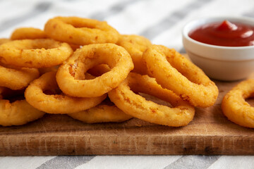 Homemade Crispy Deep-Fried Onion Rings with Ketchup on a rustic wooden board, low angle view. Close-up.