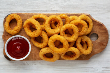 Homemade Crispy Deep-Fried Onion Rings with Ketchup on a rustic wooden board, top view. Flat lay.