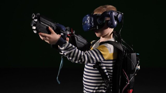 A teenage child using a VR headset helmet and an automatic controller for an imitation game on a black background. A modern child is playing a virtual game. Immersion in virtual reality.