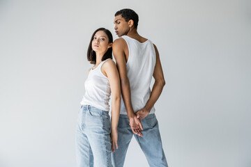 asian woman in white tank top and blue jeans looking at camera near young african american guy...
