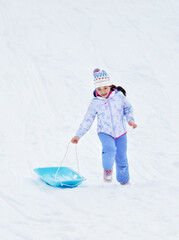 Sledding in winter.Happy little girl by the rope holds the sled and runs down the slope.