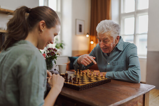 Senior man playing chess with his granddaughter.